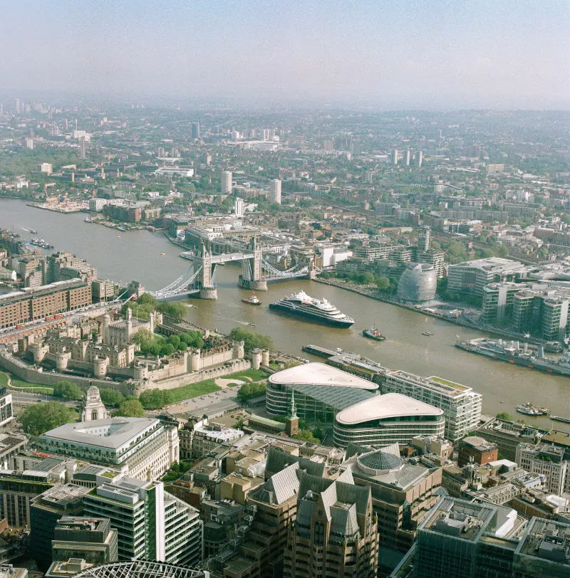 A cityscape with a bridge over a river and a large building with a green roof.