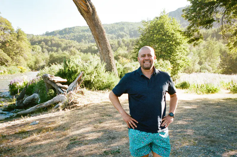 A man wearing blue shorts and a blue shirt stands in front of a tree.