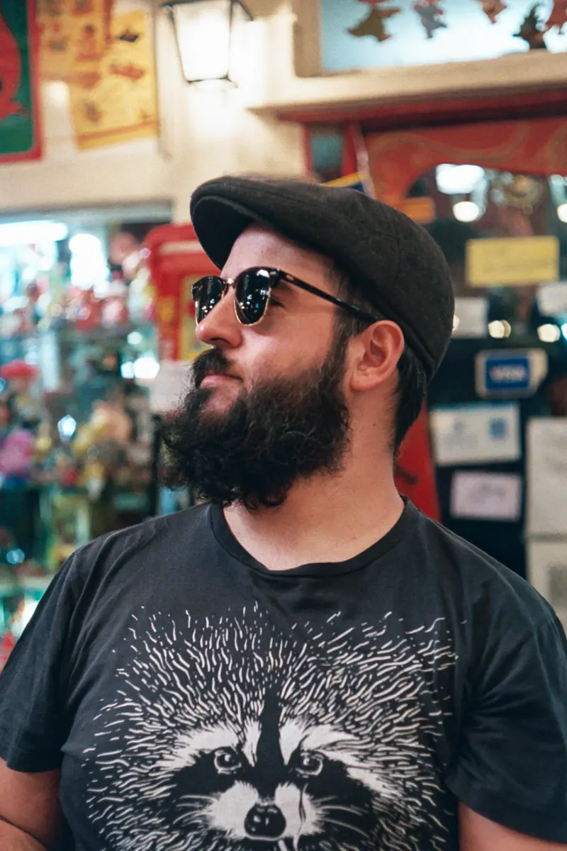 A man with a beard and sunglasses is wearing a hat.