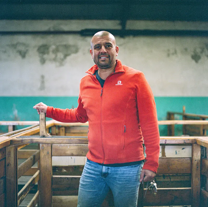 A man wearing a red jacket stands in front of a wooden fence.