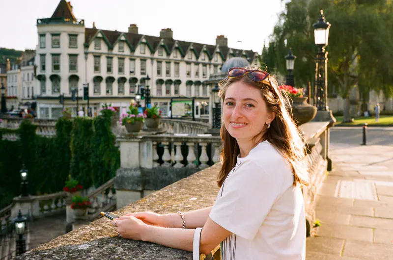 A woman wearing sunglasses and a white shirt is sitting on a bridge.