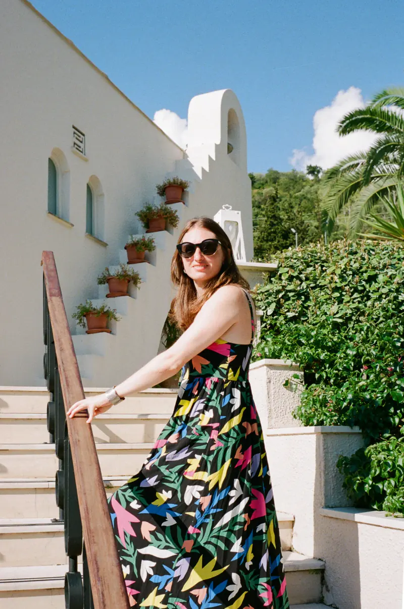 A woman wearing sunglasses and a colorful dress is standing on a staircase.