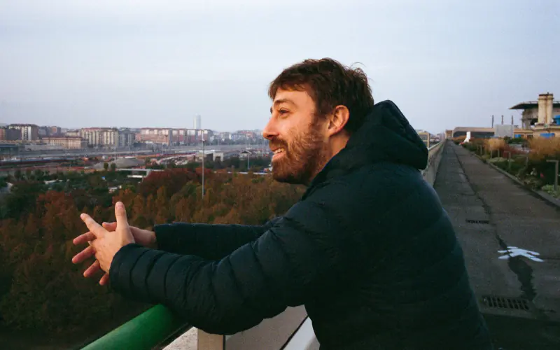 A man with a beard and mustache is leaning on a railing.