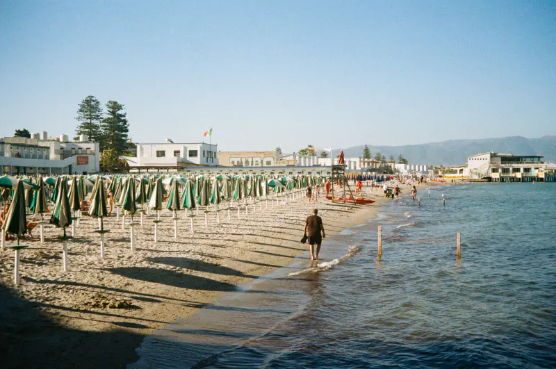 A man walks on the beach in front of a row of beach umbrellas.