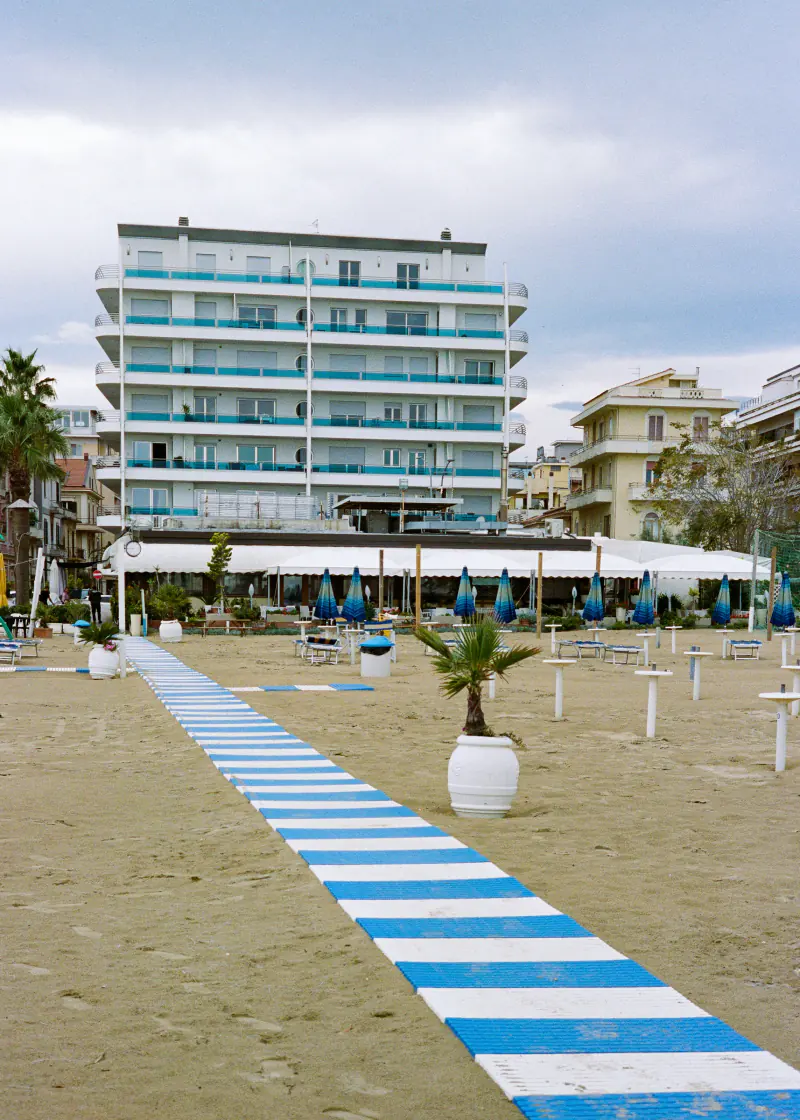 A beach with a blue and white striped path leading to a building.