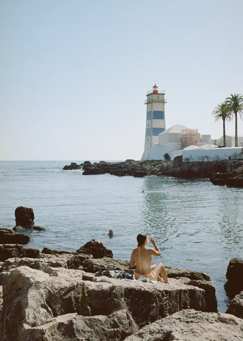 A woman is sitting on rocks near the water, looking at the ocean.