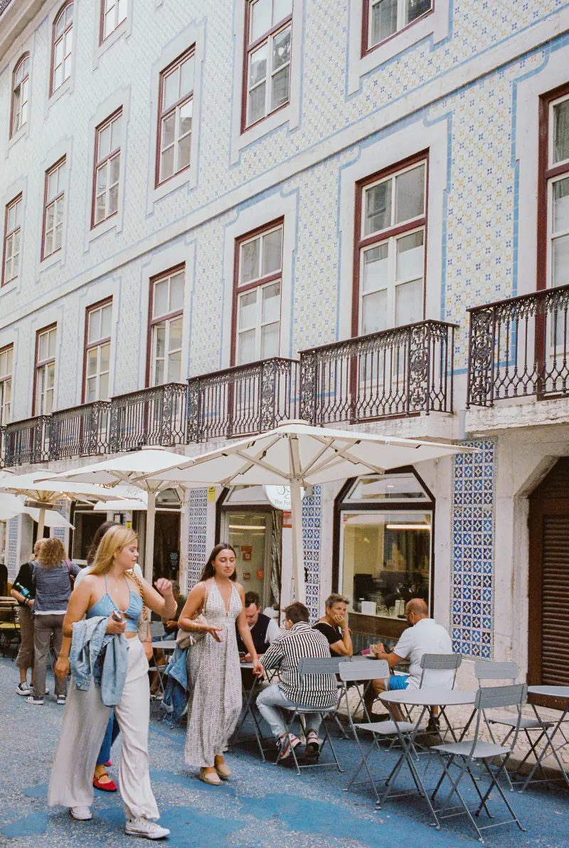 A group of people are sitting outside a building, under umbrellas.