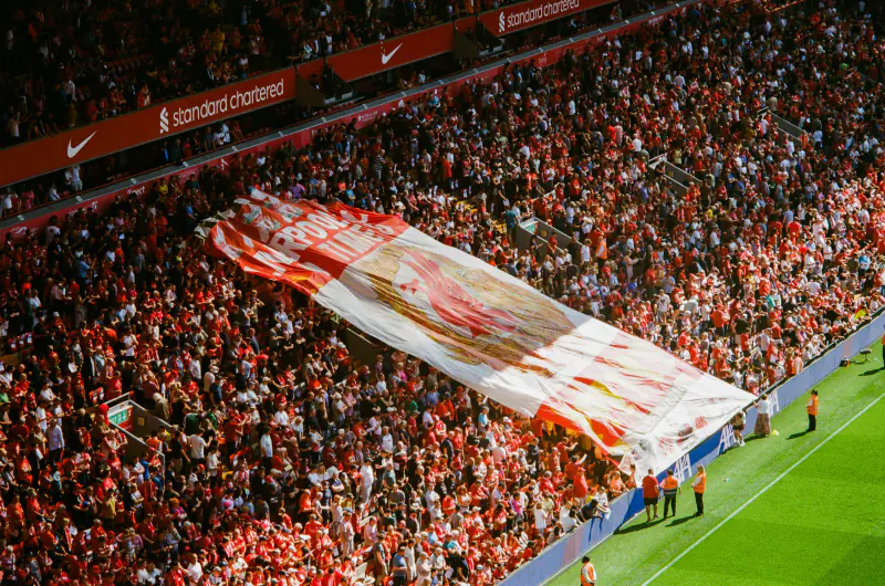 A large crowd of people are gathered in a stadium, with a banner that says "Manchester United" in the foreground.