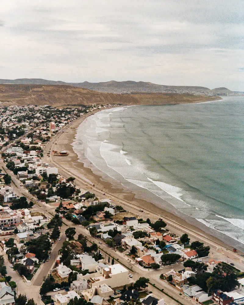 A city is situated near a beach with a mountain range in the background.