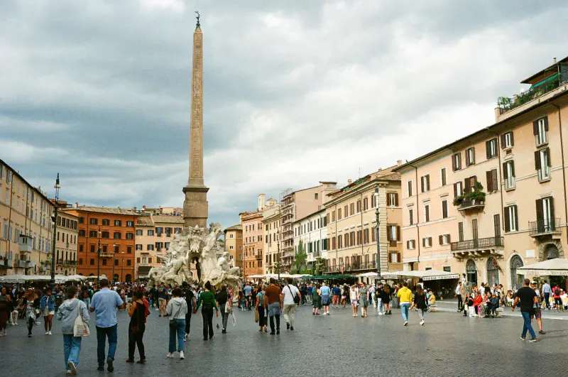 A large group of people walking on a cobblestone road in front of a tall building.